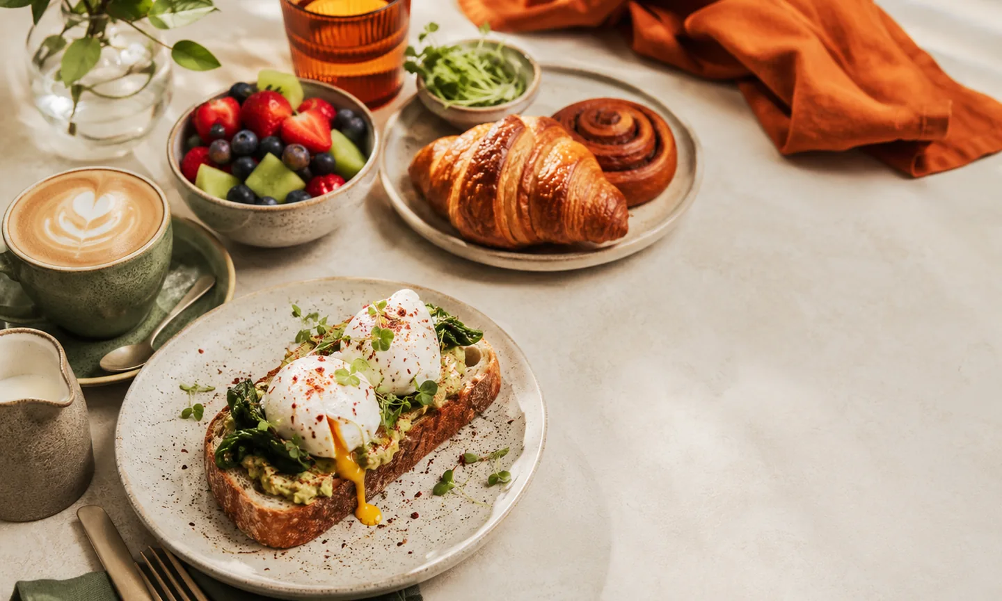 Illustrative brunch spread with poached eggs, pastries, fruit and coffee in warm natural light